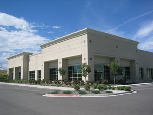 a glass and stucco building with small trees and bushes surronding it